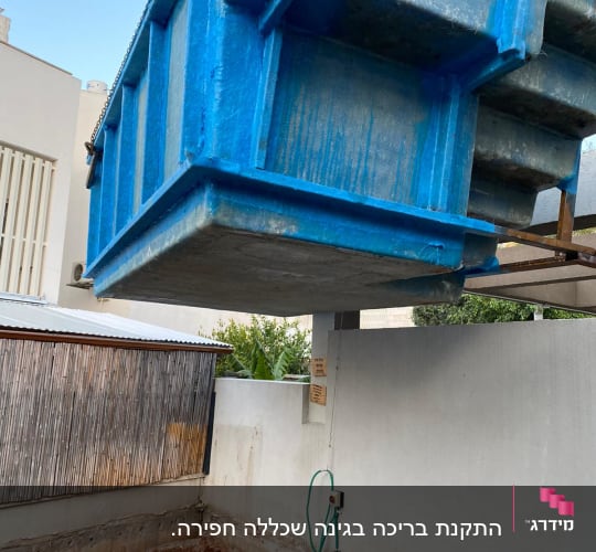 מכולה כחולה תלויה מעל חפירה באתר שיפוצים